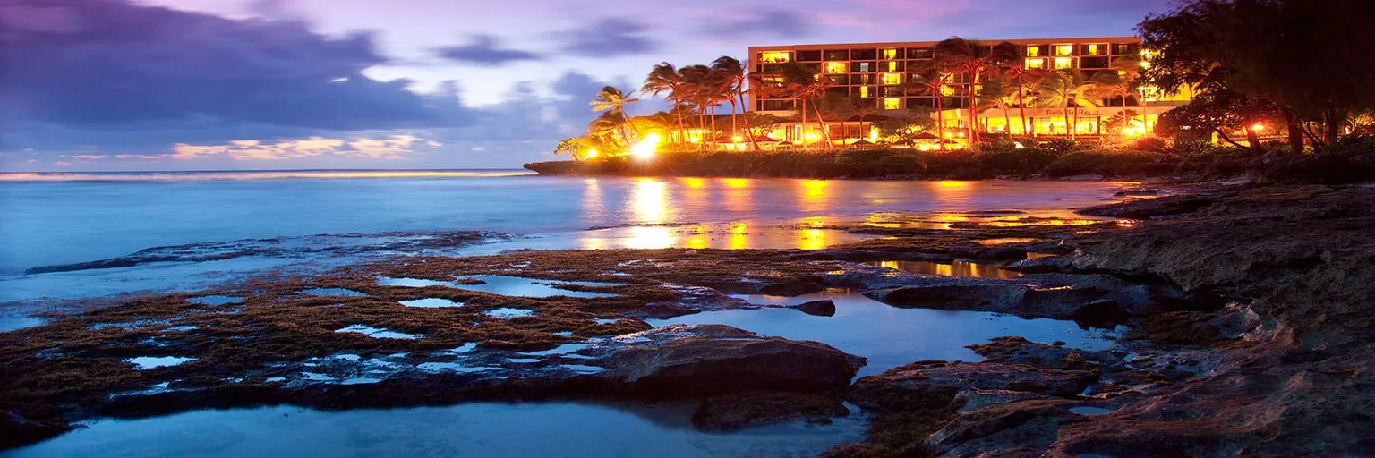 Turtle Bay Resort illuminated at twilight with palm trees and Pacific Ocean sunset